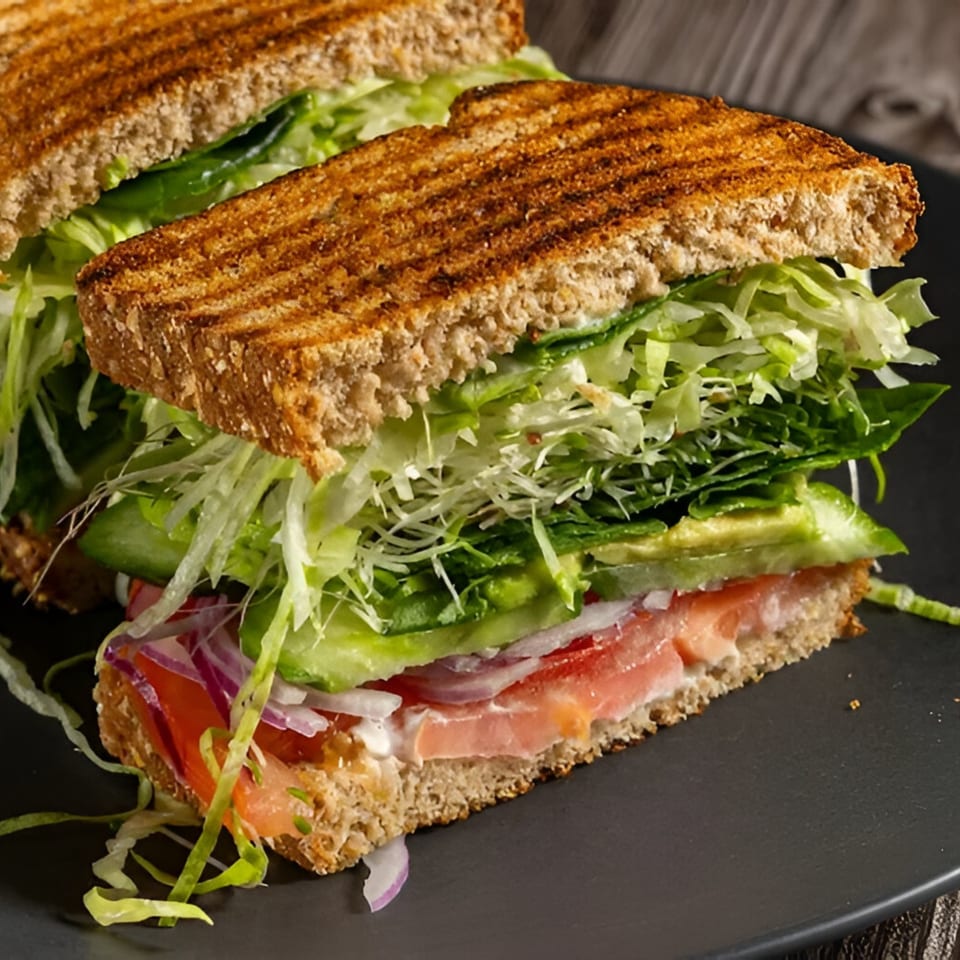 Toasted sandwich with lettuce, avocado, tomato, and red onion on a dark plate.