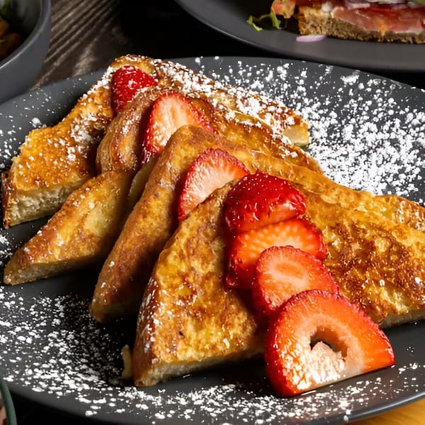 Golden French toast triangles, dusted with powdered sugar and topped with fresh strawberry slices.