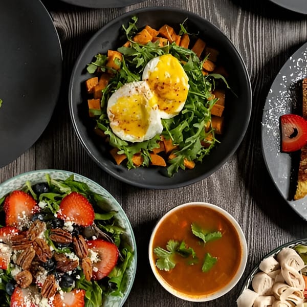 Overhead view of various dishes, including a salad with strawberries, a bowl of soup, and poached eggs.
