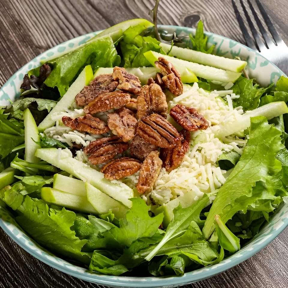 A vibrant salad with green apples, candied pecans, and shredded cheese in a blue patterned bowl.